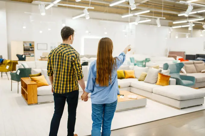 Happy couple choosing furniture in store showroom. Man and woman looking samples for bedroom in shop, husband and wife buys goods for modern home interior. Happy couple choosing furniture in store