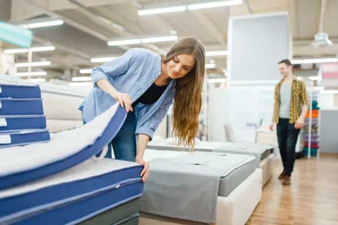 Young smiling couple in furniture store showroom. Man and woman looking samples for bedroom in shop, husband and wife buys goods for modern home interior. Young smiling couple in furniture store showroom