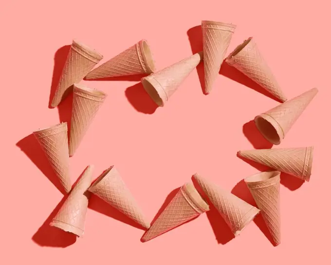 Frame from sweet wafer cones for dessert empty on a color background of the year 2019 Living Coral Pantone, place for your text. Spring or summer food concept. Top view.. Waffle sweet cones pattern on a color background of the year 2019 Living Coral Pantone. Place for text. Flat lay.