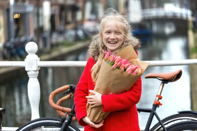 happy girl holding a bouquet of tulips sitting on a bench on a street of Amsterdam. The Netherlands