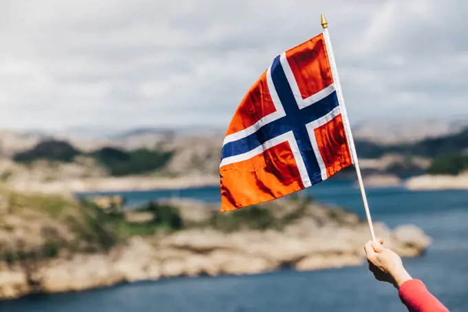 Tourist hand holding norwegian flag on rocky stone sea coast background.. Tourist with norwegian flag on sea coast