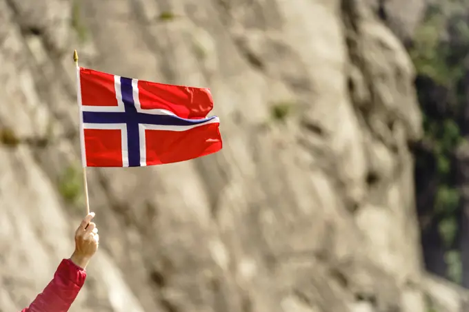 Tourist hand holding norwegian flag on rocky stone mountains background.. Tourist with norwegian flag in rocks mountains