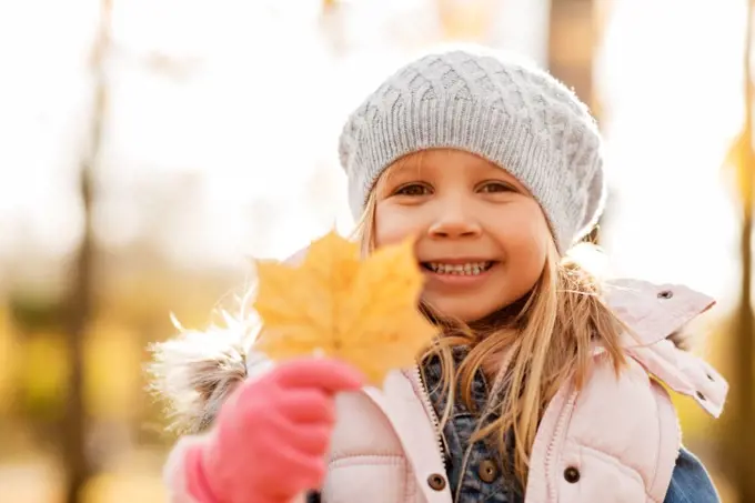 childhood, season and people concept - happy little girl with maple leaf at autumn park. happy little girl with maple leaf at autumn park