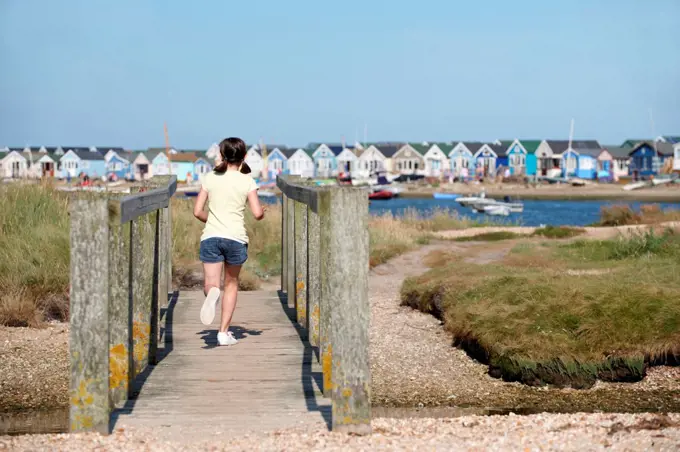 young girl running over foot bridge away from camera with beach huts in backgrounds