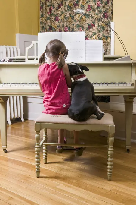 Girl and pet dog sitting on piano bench