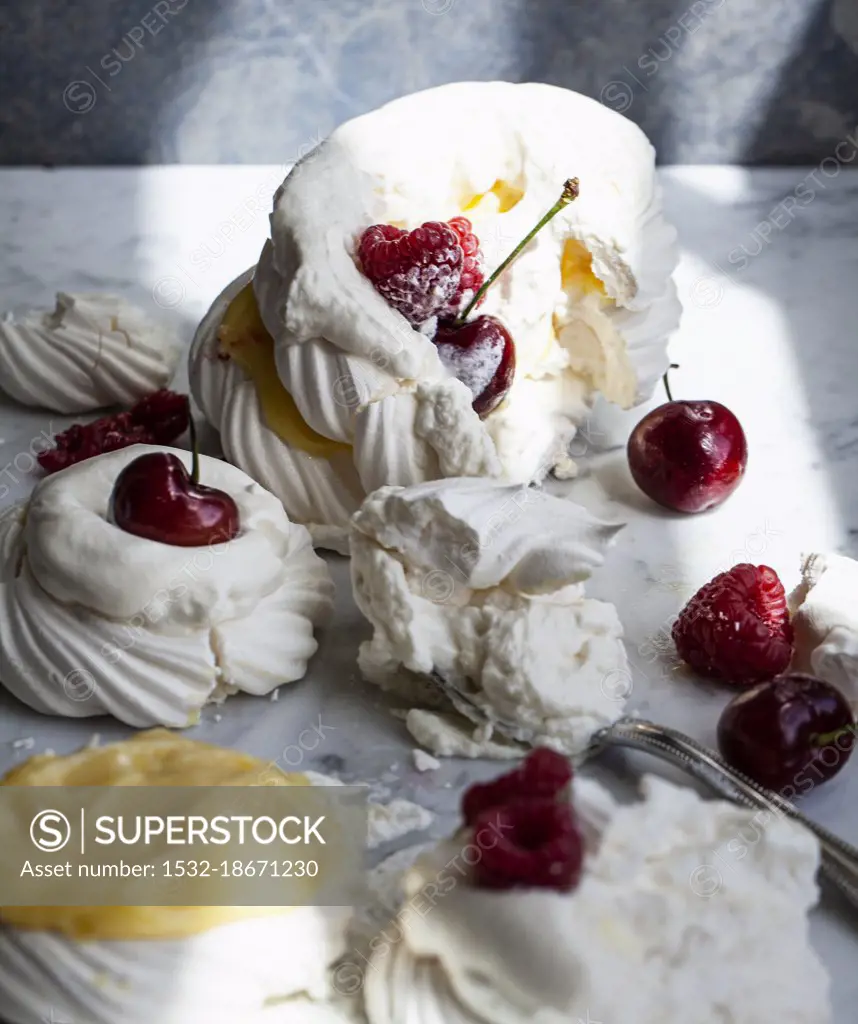 A tower of meringues topped with lemon curd, raspberries, whipped cream and cherries that has been toppled over