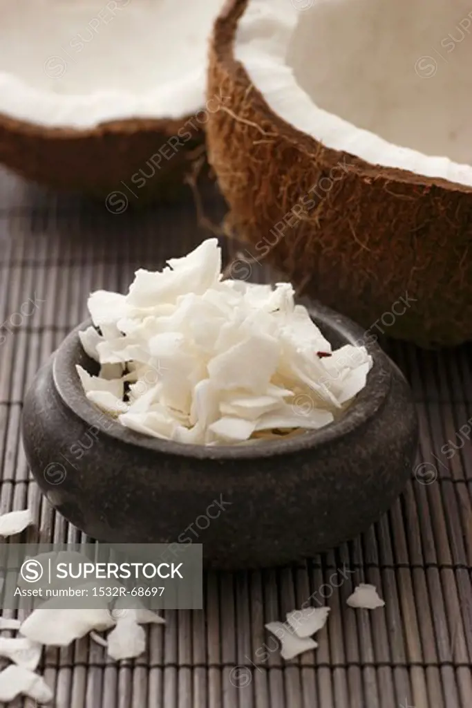 A coconut, broken open, and coconut shavings, on a bamboo mat (close-up)