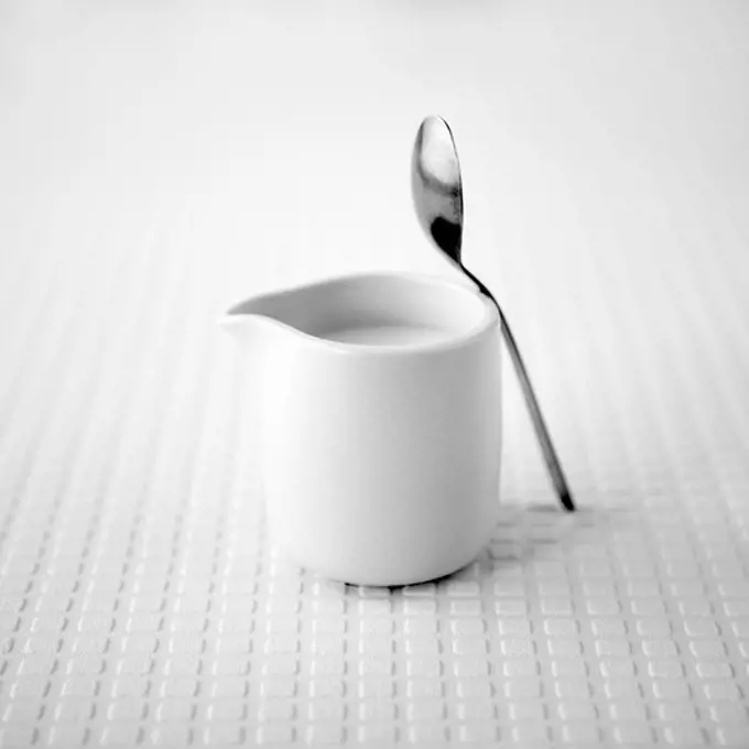 White jug of milk with a teaspoon on a white textured background, 8/2/2013