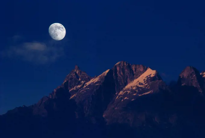 Moon over snow covered peaks , sangla valley , manali , himachal pradesh , india