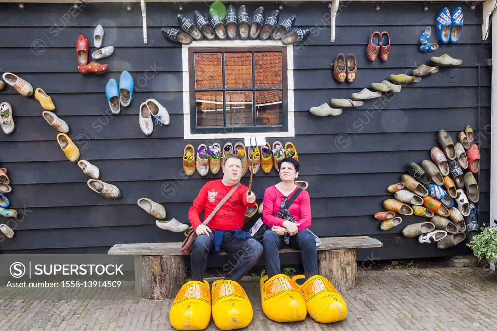 Europe, Netherlands, Zaandam, Zaanse Schans, Tourist Couple Posing with Giant Clogs