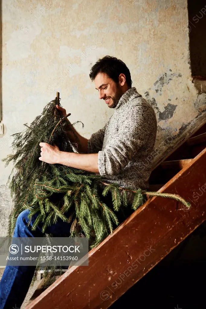 Man with knitted pullover, twigs of evergreens for decoration, stairs, sit, sitting, half-portrait, side view,