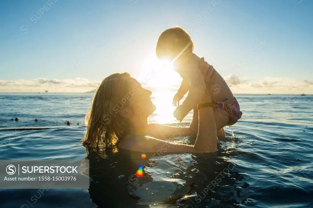 Woman playing with her little baby in a swimming pool at sunset, Papeete, Tahiti, French Polynesia