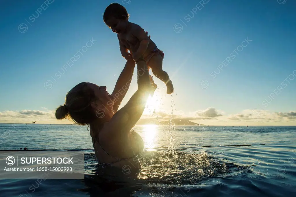 Woman playing with her little baby in a swimming pool at sunset, Papeete, Tahiti, French Polynesia