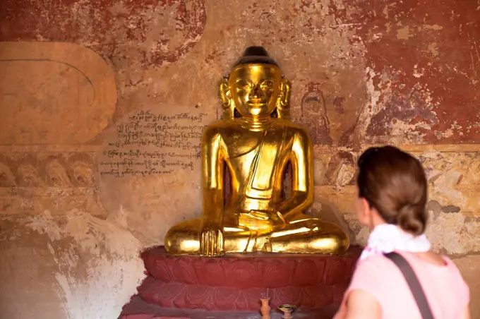 European tourist looking at golden Buddha statue in Bagan, Myanmar