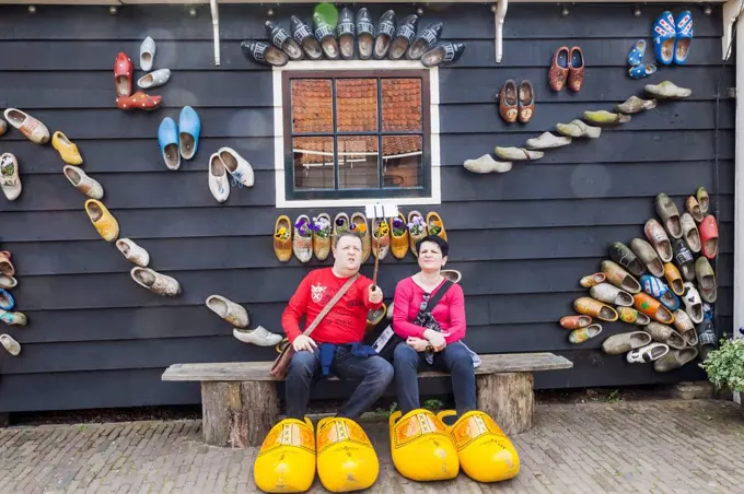 Europe, Netherlands, Zaandam, Zaanse Schans, Tourist Couple Posing with Giant Clogs