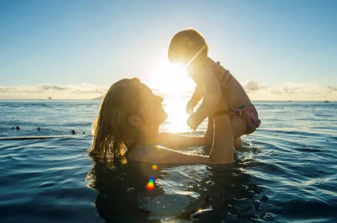 Woman playing with her little baby in a swimming pool at sunset, Papeete, Tahiti, French Polynesia