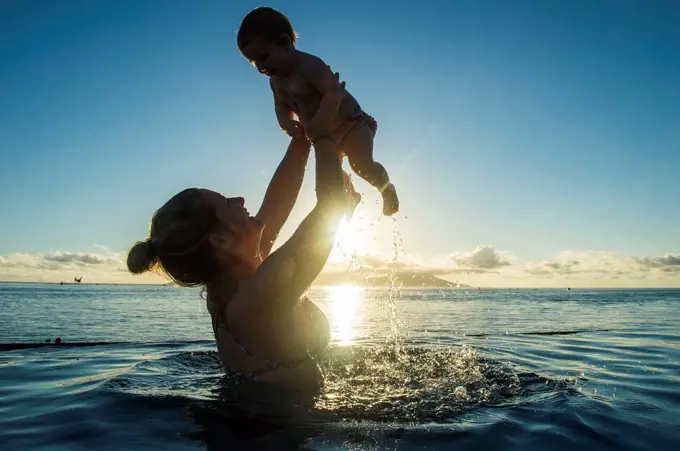 Woman playing with her little baby in a swimming pool at sunset, Papeete, Tahiti, French Polynesia