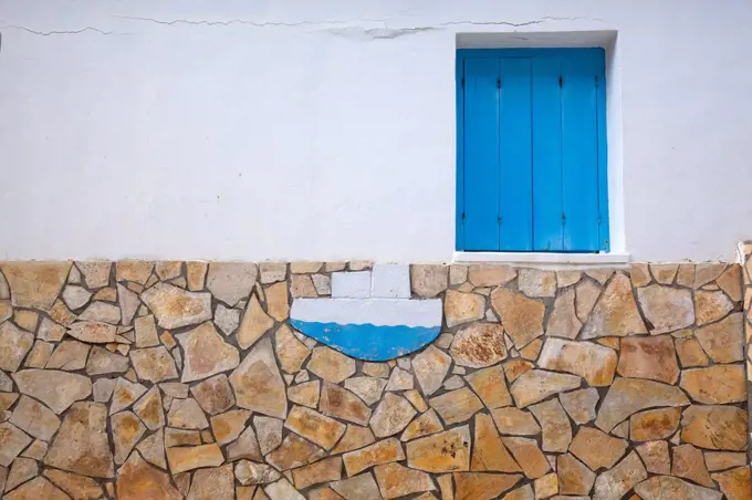 House wall with blue window and boat on quarrystone disks in Greece