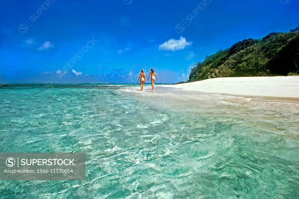 Two women walk naked on the white sand Caribbean beach in the Tobago Cays Marine Park, St. Vincent and the Grenadines