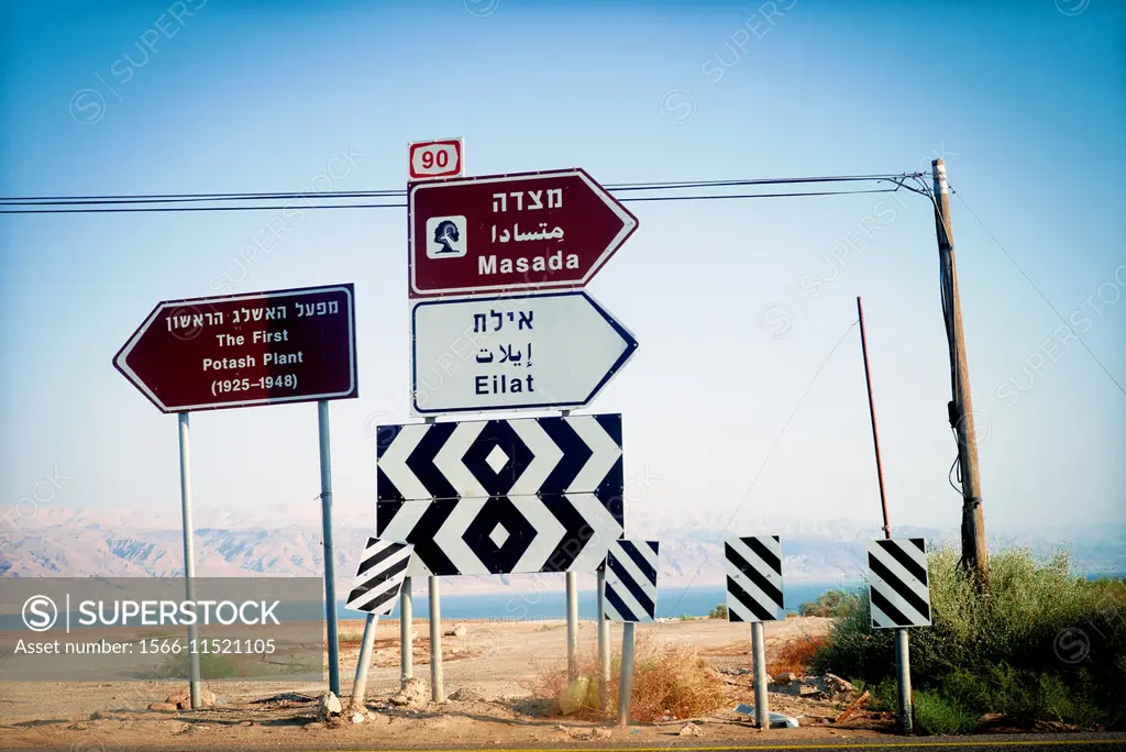 View of a several road signs indicating different places: Masada, Eilat and the first Potash Plant (1925-1948), with the Death sea on the background, ...