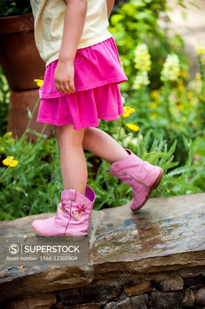 Partial of a young girl wearing pink boots and a pink skirt walking on a stone wall.