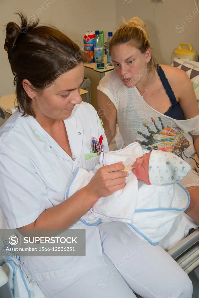 nurse feeds new born baby with milk on hospital bed as mother watches