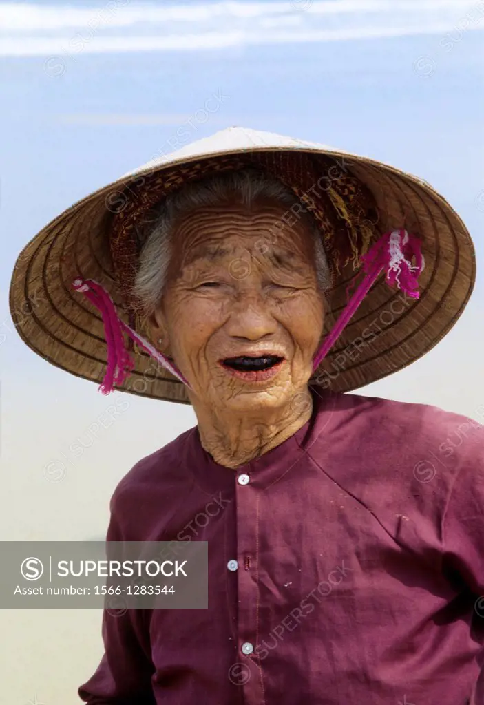 Hoi An; Beach; old Woman; Traditional Costume; Woman wearing traditional conical Hat; Vietnam.