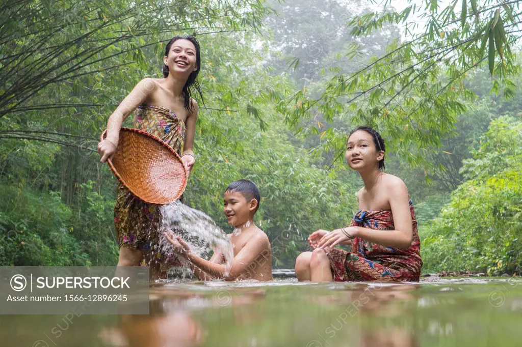 Bidayuh boy and girls in sarong playing with water, Annah Rais hot spring, Sarawak, Malaysia.