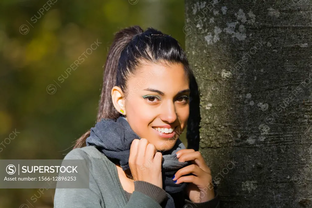 Mulatto happy portrait teen girl in forest inclined on tree