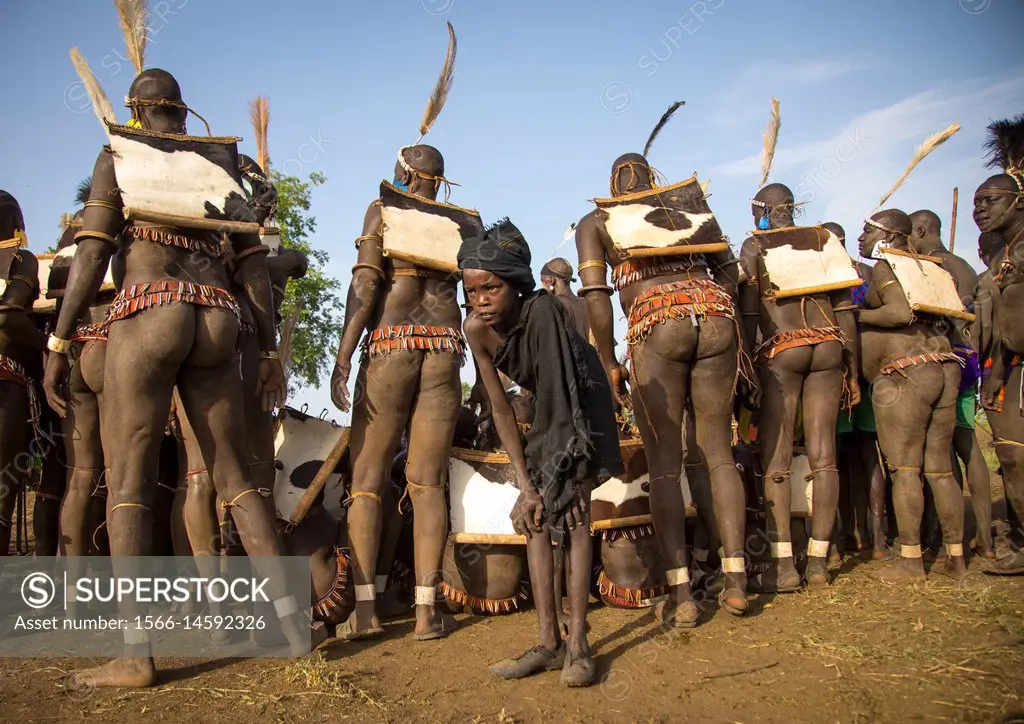 Child boy in front of Bodi tribe fat men during Kael ceremony, Omo valley, Hana Mursi, Ethiopia.