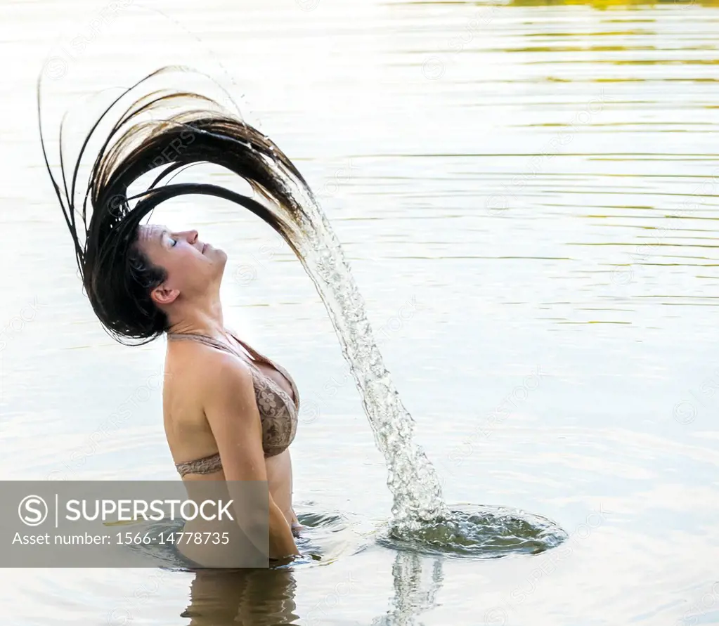 A pretty partially nude 39 year old brunette woman flipping her hair back  standing in a lake. - SuperStock