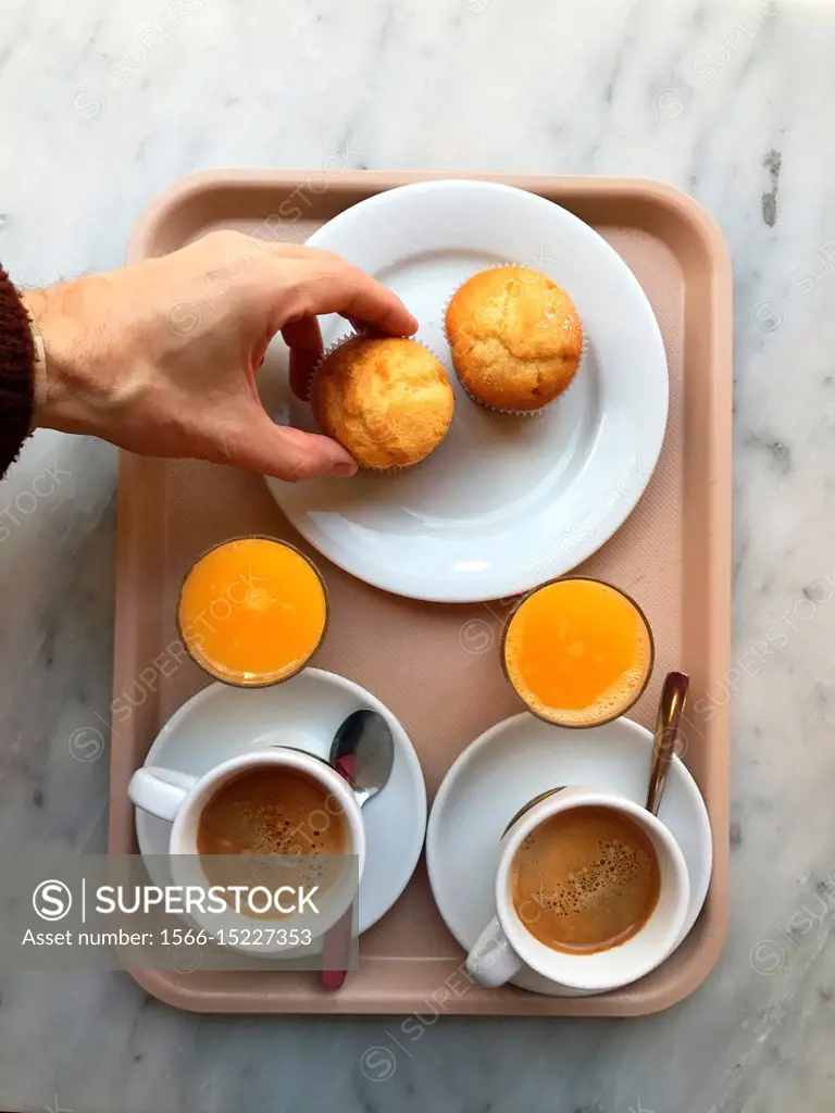 Two cups of coffee, two glasses of orange juice and two sponge cakes on a  tray, and man. . s hand taking one of the sponge cakes. View from above. -  SuperStock