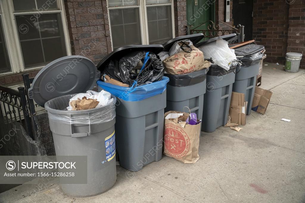 Green trash can with overflowing trash, in front of a building