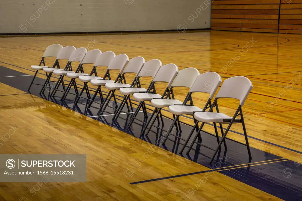 Folding chairs lined-up in a row in the middle of an empty gymnasium.