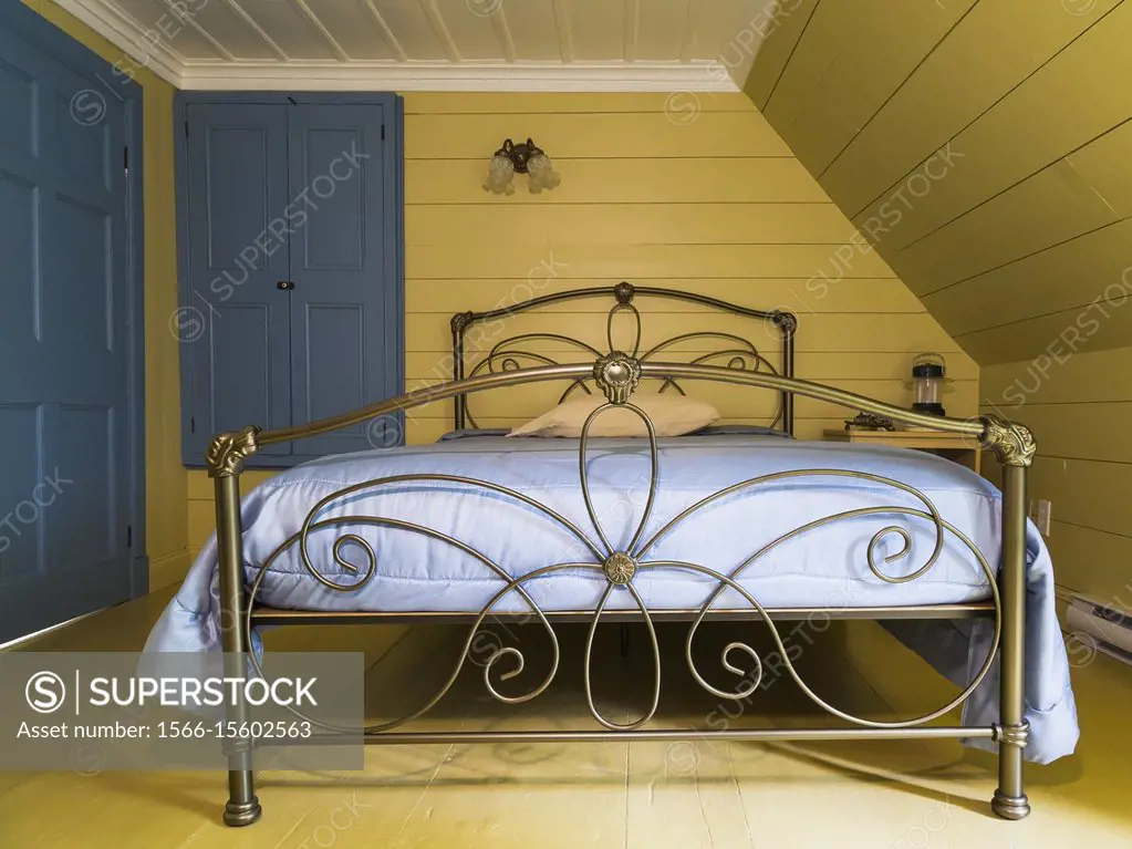 Double bed with antique brass metal headboard and footboard in upstairs  master bedroom inside an old 1809 French regime cottage style home -  SuperStock