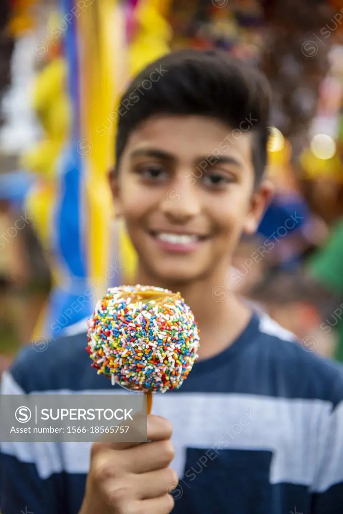 A 12-year-old boy holds a colorful caramel apple covered in sprinkles at a county fair in Arlington, Virginia.