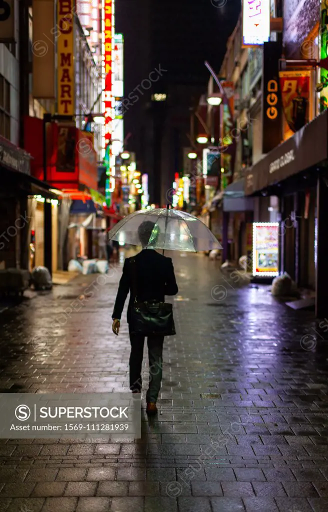 Man walking in rain with umbrella at night