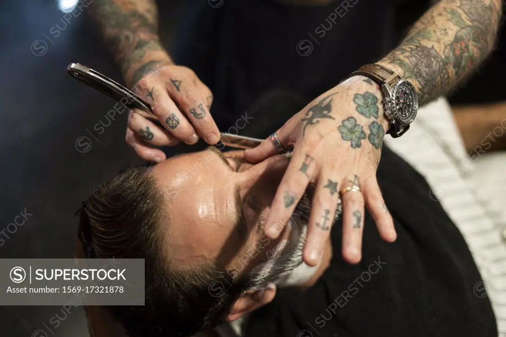 Hairdresser shaving man's beard in salon