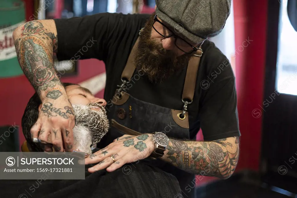 Hairdresser shaving man's beard in salon