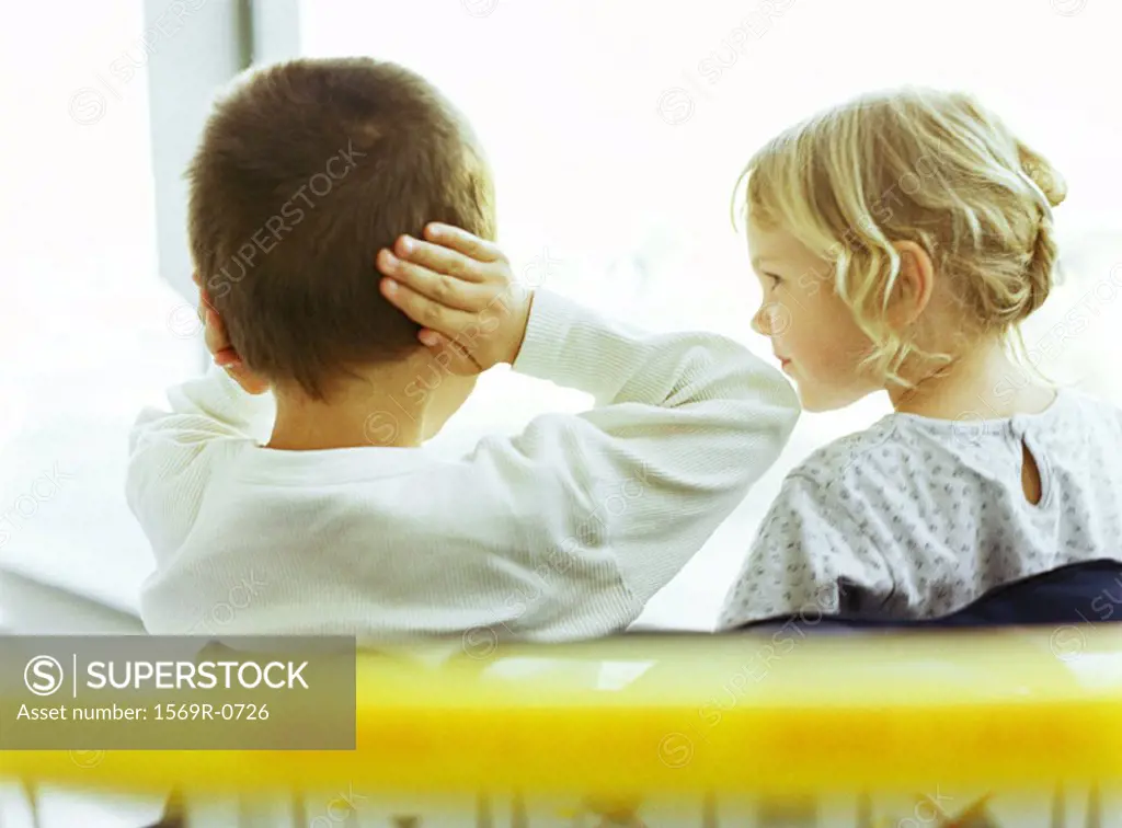 Boy and girl, boy covering ears, girl looking at boy, rear view