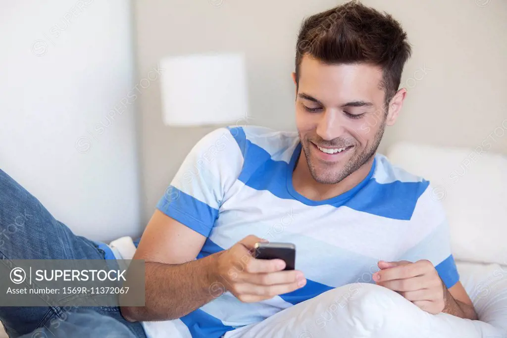 Young man reclining on bed looking at smartphone