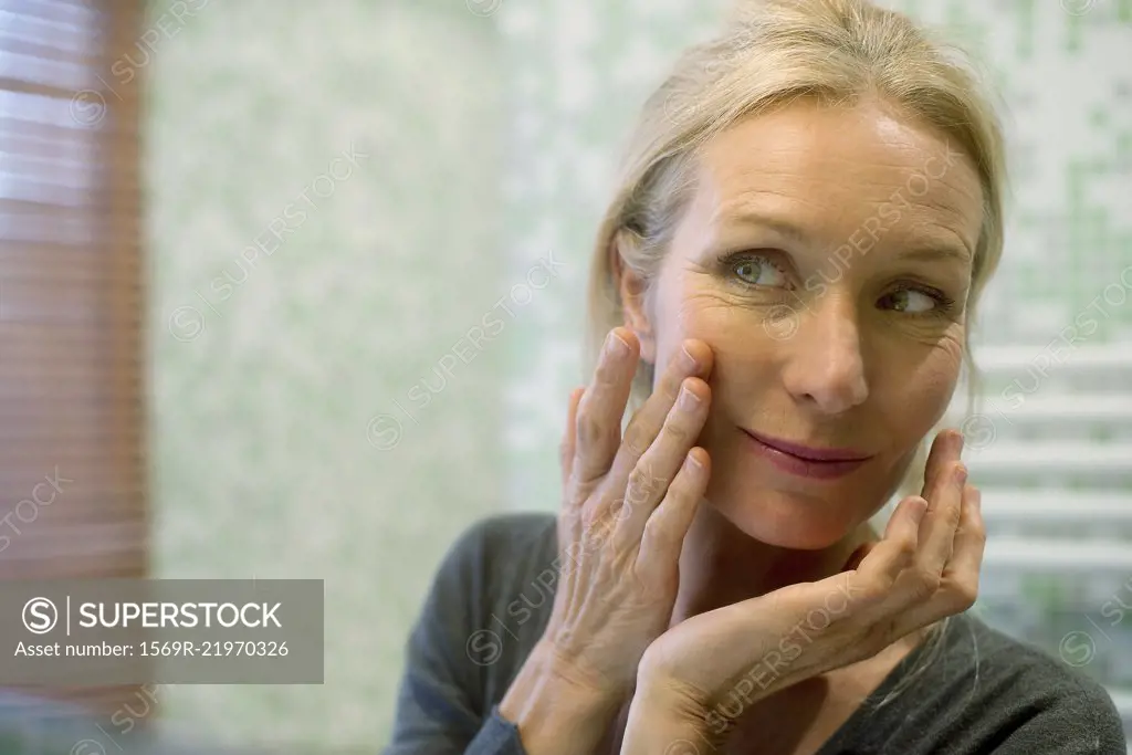 Mature woman looking at reflection in mirror with hand on cheek