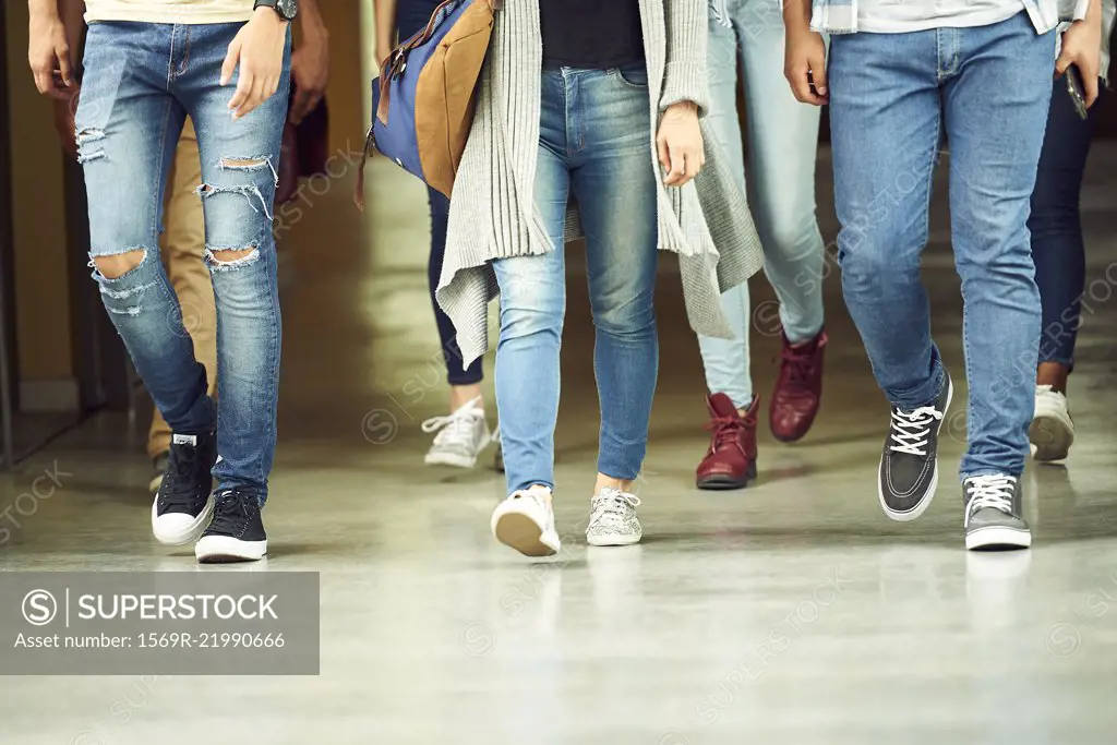 Students walking in school corridor, low section