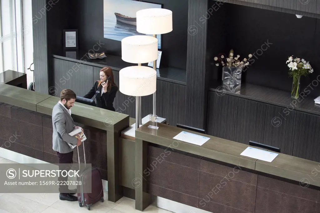 Female receptionist talking on telephone while businessman standing at counter