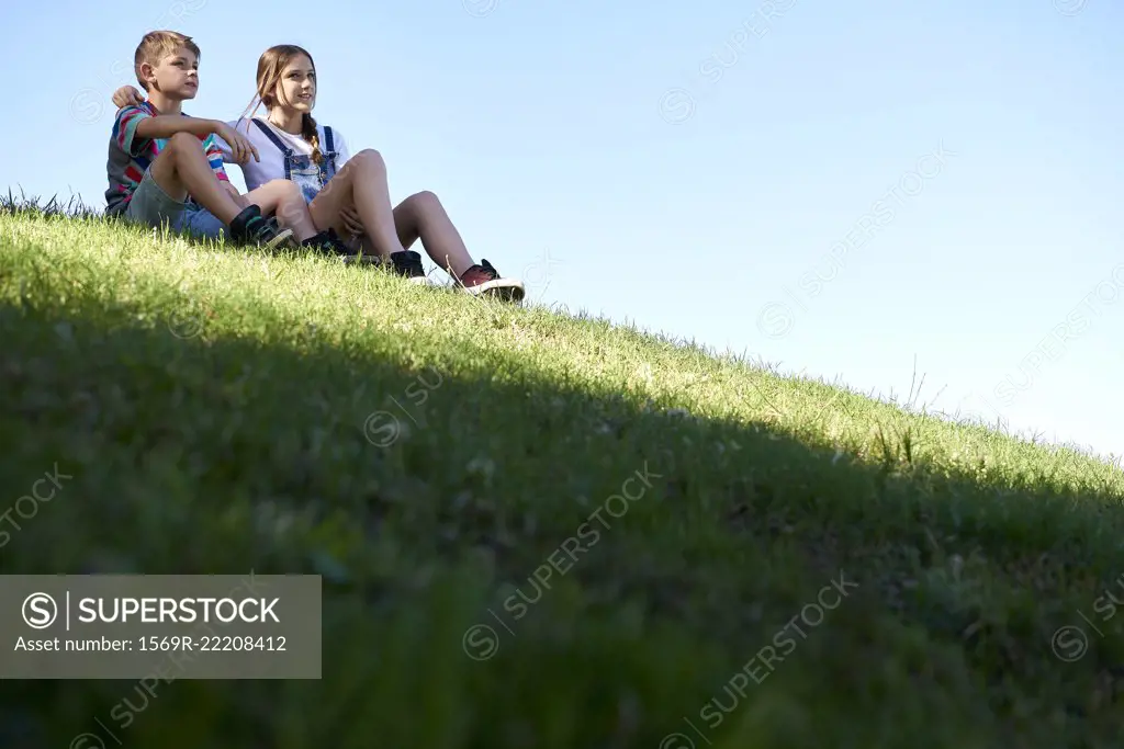 Brother and sister sitting on a grassy hill