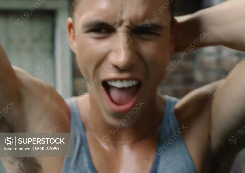 Sweaty man standing with arms up and mouth open, close-up, blurred