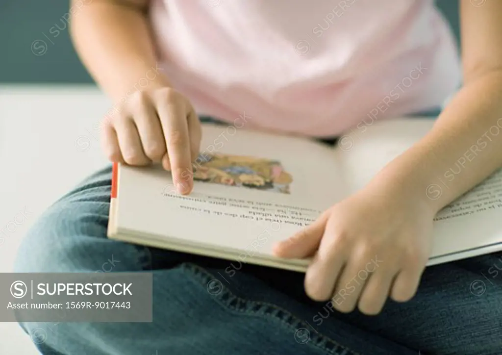 Child reading book, pointing to words, close-up