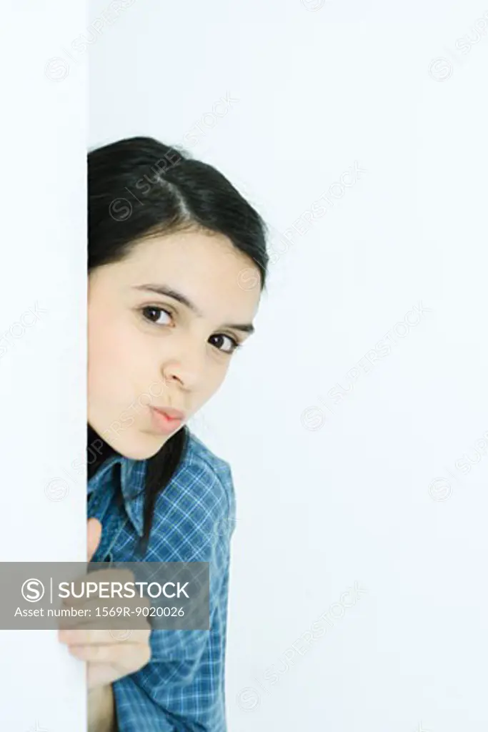 Teen girl peeking around wall, puckering at camera