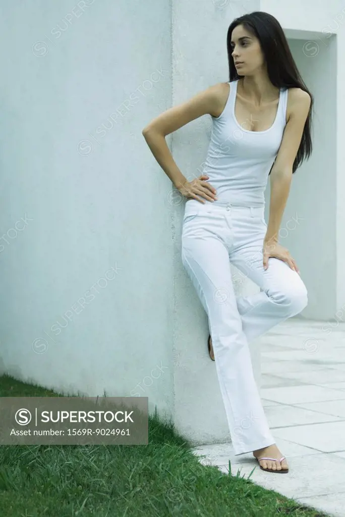 Woman standing, leaning against wall, hand on hip, looking away, full length