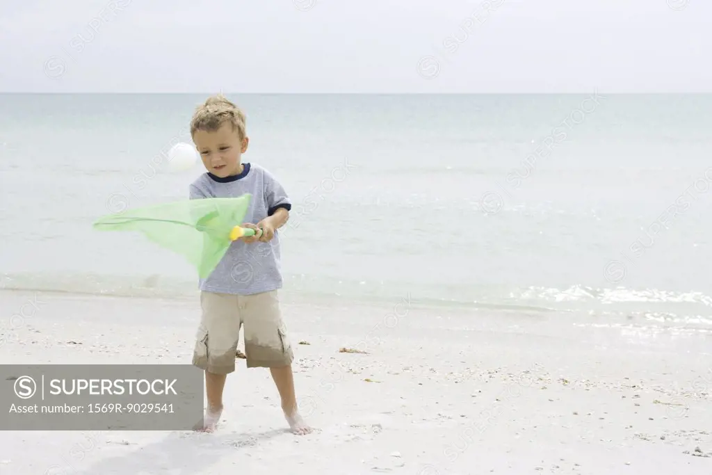 Young boy standing at the beach, trying to catch ball with net